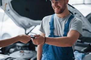 olhos fechados. mulher no salão de automóveis com funcionário de uniforme azul levando seu carro reparado de volta foto