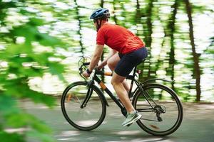 cenário rural. ciclista de bicicleta está na estrada de asfalto na floresta em dia ensolarado foto