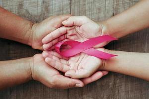 conceito de saúde e medicina. mão segurando a fita rosa na madeira. conscientização do câncer de mama. sinal de esperança foto