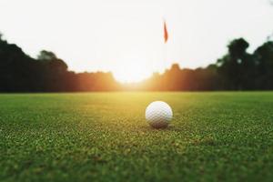 bola de golfe na grama verde com buraco e luz solar foto