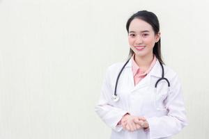 uma jovem e bela médica asiática de uniforme médico está de pé sorrindo de mãos dadas com fundo branco. novo conceito normal e de saúde foto