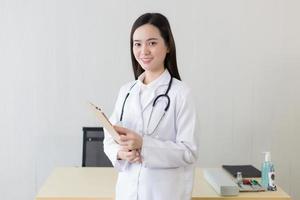médica asiática examina o documento de relatório do paciente para planejar o próximo tratamento. ela olha para a prancheta na mão enquanto trabalha no hospital. foto