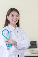médico jovem bela mulher asiática em pé com os braços cruzados feliz e sorriso no hospital. vestindo uma túnica branca e estetoscópio. conceito de cuidados de saúde. foto