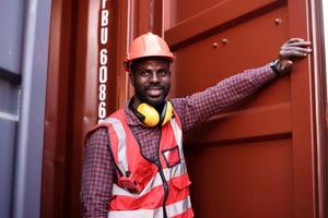 feliz engenheiro masculino afro-americano sorrindo quando ele está no armazém de contêineres, trabalhador obtém segurança social e seguro, dia do trabalho e conceito de negócio de sucesso. foto