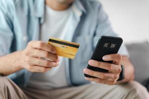 homem segurando cartão de crédito e usando smartphone para compras online, internet banking, e-commerce, gastar dinheiro, trabalhando em casa conceito foto