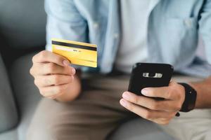 homem segurando cartão de crédito e usando smartphone para compras online, internet banking, e-commerce, gastar dinheiro, trabalhando em casa conceito foto