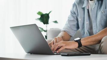 feche as mãos do homem digitando no teclado do laptop em cima da mesa no escritório em casa ou no local de trabalho. foto