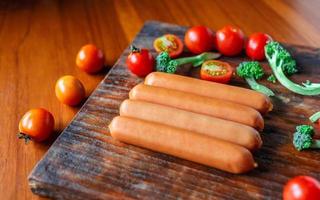 salsicha crua em uma tábua de madeira com brócolis e tomate foto