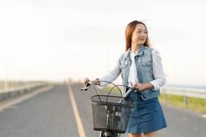 menina adolescente saudável e sincera dando um passeio com uma bicicleta na ponte no verão foto