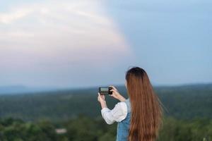 vista traseira retrato de uma mulher tirando foto de uma paisagem com um telefone inteligente