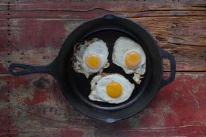 três ovos fritos do lado ensolarado em panela de ferro fundido na mesa de madeira foto