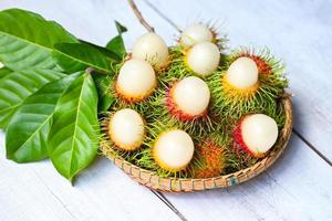 rambutan fresco e maduro doce fruta tropical descascada rambutan com folha, fruta rambutan na colheita de fundo da cesta da árvore de rambutan do jardim foto