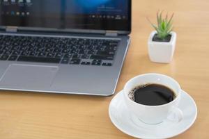 computador portátil e papel de nota com uma xícara de café na mesa de madeira foto