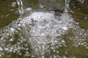 respingar gotas de água e cascata de bolhas como pano de fundo o conceito de frescura da água e bolhas de ar na superfície da água. foto