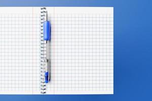 Ilustração 3D, um caderno escolar em uma gaiola e uma caneta azul sobre fundo azul, um bloco de notas em espiral em cima da mesa. papelaria escolar. de volta à escola foto