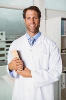 médico homem sorridente segurando livros no consultório médico