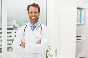 médico sorridente com os braços cruzados no consultório médico