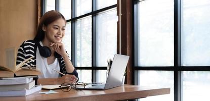 sorrindo jovem mulher asiática usando fone de ouvido olhando para a tela do laptop ouvir e aprender cursos online. mulher de negócios chinesa feliz com chamada de vídeo de fones de ouvido para atendimento ao cliente foto