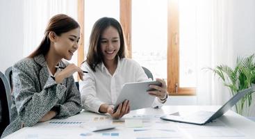 duas empresárias felizes coworking com um laptop em um desktop no escritório foto