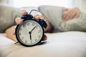 homem sonolento segurando o despertador de manhã com acordar tarde - todos os dias o conceito de vida em casa foto