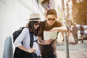 turista de casal de mochila asiática segurando o mapa da cidade atravessando a estrada - conceito de estilo de vida de férias de pessoas de viagem foto