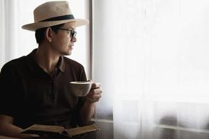 relaxe o homem asiático beba café e leia o livro em uma cafeteria de estilo moderno - pessoas com conceito de estilo de vida fácil de xícara de café foto