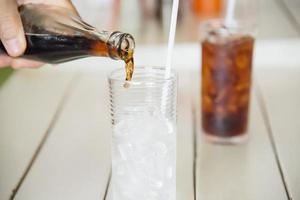 mão despeje refrigerante em um copo com gelo - conceito de bebida gelada refresco com sede foto