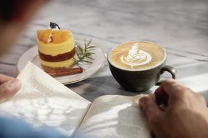 relaxe o homem asiático beba café e leia o livro em uma cafeteria de estilo moderno - pessoas com conceito de estilo de vida fácil de xícara de café foto
