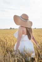 jovem de vestido branco em pé em um campo de trigo com o nascer do sol no fundo, vista traseira foto