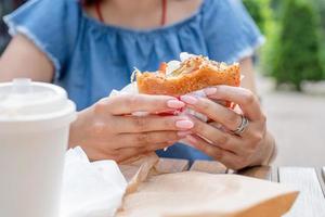 closeup de mãos de mulher segurando hambúrguer, mulher comendo fast food no café de rua foto