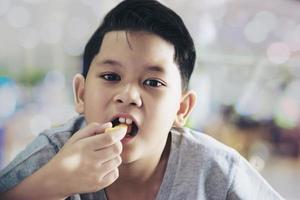 menino comendo batata frita com molho sobre mesa de madeira branca foto