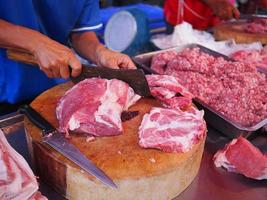 mãos de açougueiro cortando carne de porco em pedaços para o mercado fresco foto