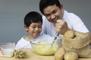 papai e filho fazendo purê de batata alegremente foto