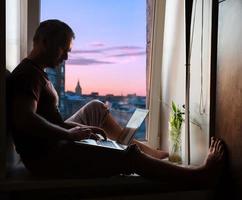 silhueta do homem no peitoril da janela com o laptop