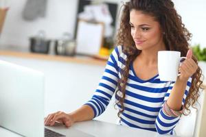 mulher jovem sorridente com uma xícara de café e laptop no