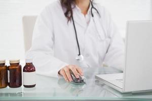 médico usando laptop perto de frascos de comprimidos foto