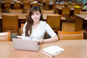 bela aluna asiática usando laptop para estudo na biblioteca