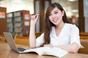 bela aluna asiática usando laptop para estudo na biblioteca