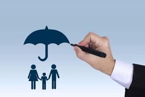 mão de empresário desenhando um guarda-chuva acima de um conceito de família para proteção, segurança, finanças e seguros foto