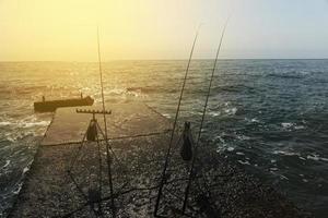 três varas de pesca são colocadas no cais com o mar ao fundo. o conceito de esperar por uma mordida. foto