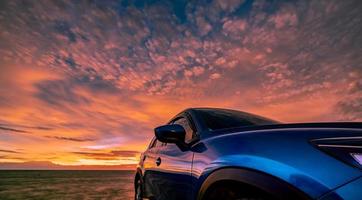 carro suv compacto azul com design esportivo, moderno e luxuoso estacionado na estrada de concreto à beira-mar ao pôr do sol. vista frontal do belo carro elétrico. dirigindo com confiança. viajar de férias na praia. foto