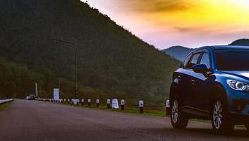 carro suv azul estacionado na estrada de asfalto em frente à montanha. carro estacionado no parque no início da manhã com céu ao nascer do sol. viagem de viagem. vaga de estacionamento. indústria automobilística. turismo de natureza. foto