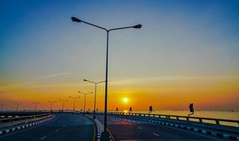 estrada costeira curvada com lâmpada de rua e céu laranja ao pôr do sol em chonburi, tailândia. foto