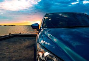 carro suv compacto azul com esporte e design moderno estacionado na estrada de concreto à beira-mar ao pôr do sol à noite. conceito de tecnologia de carro híbrido e elétrico. vaga de estacionamento. indústria automobilística. foto