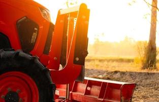 trator laranja estacionado na fazenda de arroz na manhã de verão com luz solar. máquinas agrícolas na fazenda agrícola. conceito de agricultura inteligente. veículo na fazenda. máquinas que economizam mão de obra. equipamentos para plantação foto