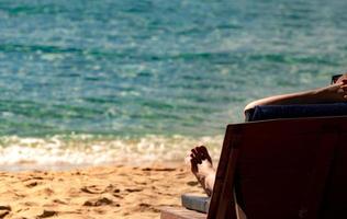 aproveite e relaxe a mulher caucasiana usando óculos escuros deitado e tomando sol na espreguiçadeira na praia de areia para fazer a pele bronzeada na ilha tropical do paraíso. férias de verão na praia. conceito de agente de viagens de férias. foto