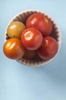 tomate cereja em uma tigela sobre fundo azul de madeira foto