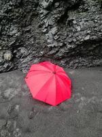 um guarda-chuva vermelho solitário nas intermináveis praias negras da Islândia em frente a formações rochosas de basalto negro. foto