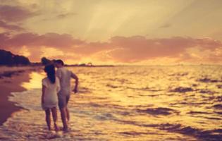 foto estilo vintage borrão casal asiático correndo na praia ao pôr do sol.