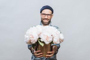 estas flores são para você feliz sorridente homem barbudo estica as mãos enquanto segura um monte de lindas flores brancas, faz presente para alguém, isolado sobre o fundo do estúdio, tem um encontro com a namorada foto